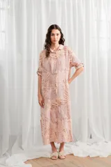 Túnica de lino con estampado de hojas en tonos rosados y beige, corte holgado, cuello camisero y cierre frontal con botones. Mangas largas con opción de enrollar y abotonar.