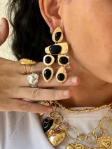 Aros colgantes dorados con incrustaciones de piedras negras de diferentes formas geométricas.