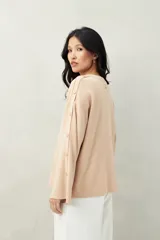 Sweater color beige de tejido de punto, con cuello redondo y mangas largas acampanadas con botones decorativos en los laterales.