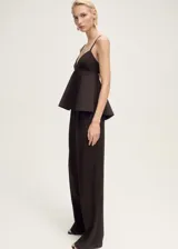 Top negro con tirantes finos, escote en pico y bajo con volantes. Cierre de gancho en la parte posterior y abertura en la espalda.