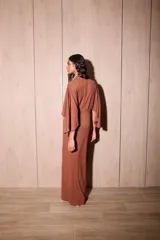 Vestido largo tipo kimono de color marrón, confeccionado en tela de punto texturada. Posee mangas amplias y abiertas, escote en V pronunciado y un lazo ajustable en la cintura para definir la silueta.