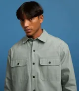 Camisa marrón de manga larga, confeccionada en sarga, con cuello inglés, abotonado delantero, bolsillos en el pecho con solapa y puños abotonados.
