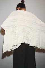 Capa color crudo de tejido texturizado, con cuello redondo y mangas cortas tipo kimono. El bajo es asimétrico.