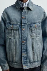 Cazadora de denim de algodón de corte regular, color azul medio lavado. Presenta cuello solapa, manga larga con puños abotonados, dos bolsillos de solapa en el pecho y bolsillos laterales en la costura de la cadera. Cierre frontal con botonadura.