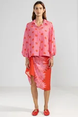 Camisa de manga larga color rosa con rayas verticales rojas y estampado de flores rojas. Tiene cuello camisero, puños elastizados y lazos regulables en los costados del ruedo.