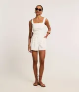 Bermuda de piquet color blanco con estampado de lunares negros, de corte recto, tiro alto, con trabillas en la cintura, pliegues y cierre tradicional.