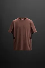 Camiseta deportiva marrón de corte relaxed fit, cuello redondo y manga corta. Presenta paneles laterales de malla negra y logo estampado en la espalda.