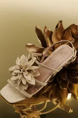 Sandalia plana color dorado con punta cuadrada y tiras finas. Presenta una flor decorativa en el empeine.