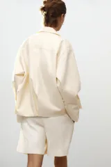 Cazadora tipo bomber color crema confeccionada en hilatura con mezcla de algodón. Cuello solapa y manga larga. Bolsillos delanteros. Forro interior a tono. Bajo ajustable. Cierre frontal con cremallera metálica.