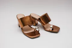 Sandalias de cuero color bronce con taco cuadrado y tira ancha sobre el empeine. Presentan un aro metálico plateado que separa el dedo gordo del resto.
