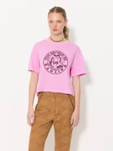 Remera rosa de algodón pima con estampado circular en el frente con la frase 'You Should Be Dancing' y un personaje bailando. Tiene corte amplio, mangas cortas, cuello redondo y tajos laterales.