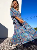 Vestido túnica largo de algodón con estampado de arabescos en tonos azules, rojos y verdes. Tiene escote en V con cordones y mangas acampanadas.
