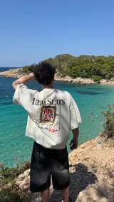 Remera marrón con estampado de un reloj dorado y la frase "Who wears a watch in Ibiza?".