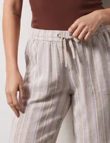 Pantalón de lino a rayas verticales color beige y blanco, con pretina ancha elastizada, lazo de ajuste y bolsillos inclinados.