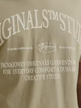 Camiseta color arena de manga corta y cuello redondo con estampado frontal con la leyenda "ORIGINALS STM STU JACK&JONES ORIGINALS GARMENTS FOR EVERYDAY COMFORT & DURAR CREATIVE STUDIO".