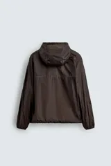 Cazadora de tejido técnico ripstop color marrón oscuro, con cuello alto y capucha ajustable, mangas largas con puños elásticos, bolsillos frontales con cremallera oculta, bajo ajustable con elástico lateral y cierre frontal con cremallera.