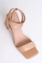 Sandalia de cuero color nude, con tira delgada sobre los dedos, pulsera al tobillo con hebilla y tacón cuadrado.