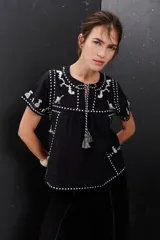 Blusa negra con bordados blancos de animales y motivos geométricos. Tiene cuello redondo con lazo y mangas cortas.