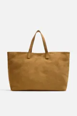 Bolso tipo shopper color marrón claro, fabricado en piel con acabado serraje. Tiene un compartimento principal con cierre imantado y un bolsillo interior con cremallera. Cuenta con dos asas de mano fabricadas en piel.