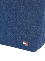 Cartera tipo tote confeccionada en tejido denim azul de Tommy Jeans. Presenta asas de hombro ajustables con hebillas metálicas y ojalillos, un compartimento principal y el logo de la bandera de Tommy Jeans en una placa metálica frontal.