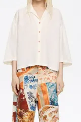 Camisa color crema de corte boxy, confeccionada en mezcla de lino, con cuello camisero, manga 3/4 con sisa ajustable y cierre con botonadura frontal.