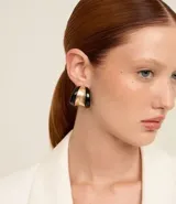 Caravanas de aro con diseño curvado y orgánico, presentan un contraste de acabado brillante en colores negro y dorado. Cuentan con cierre de perno y tuerca.