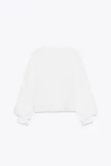 Blusa blanca de cuello solapa y manga larga abullonada terminada en volantes. Presenta bordados florales calados en el frente y cierre frontal con botones.