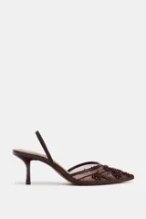 Zapato de tacón alto, destalonado, con punta fina. El cuerpo del zapato es de malla (mesh) color marrón oscuro, con apliques bordados y brillos en tonos similares. Posee una tira trasera elástica para ajuste.