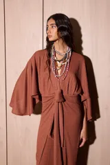 Vestido largo tipo kimono de color marrón, confeccionado en tela de punto texturada. Posee mangas amplias y abiertas, escote en V pronunciado y un lazo ajustable en la cintura para definir la silueta.