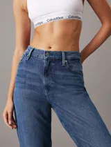 Pantalón de jean azul de corte mom, tiro alto, pierna recta y tobillo ajustado. Confeccionado con denim comfort stretch de peso medio, con un 20% de algodón reciclado. Cuenta con bragueta con cremallera, diseño de cinco bolsillos, herrajes de Calvin Klein e insignia de Piel.