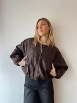 Campera marrón de cuero sintético, corte holgado, con cierre frontal y mangas largas con puños elásticos.