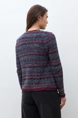 Chaqueta corta de tejido bouclé o tweed, sin cuello ni cierre frontal, con ribetes en color bordó. El tejido es una mezcla de hilos en tonos azul marino, rojo/bordó y blanco, creando un efecto jaspeado. Los puños tienen un detalle de flecos en color bordó.