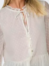 Blusa blanca con textura de lunares, cuello con volantes y lazo, cierre frontal con botones, mangas largas abullonadas con puños elásticos y corte peplum.