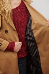 Trench coat largo color beige con doble botonadura, cuello solapa, cinturón ajustable y puños con tiras.