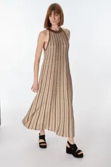 Vestido largo de tejido de punto en hilado fino con lurex, color beige con rayas verticales marrones. Tiene cuello halter y silueta en A.