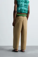 Pantalón color beige de corte ancho, con pliegues frontales dobles, bolsillos laterales y traseros de vivo. Largo cropped y cierre frontal con cremallera y botón.
