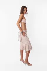 Conjunto de top y short color beige confeccionado en tela brillante. El top cuenta con arco metálico en el busto, tiras para atar en el hombro y ganchos lenceros en la espalda. El short es de tiro alto con cintura elastizada y bolsillos laterales.
