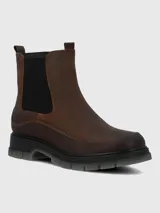 Botín Chelsea de mujer color marrón oscuro, con caña corta, elástico lateral negro y suela track gruesa de goma negra con una capa exterior translúcida gris.