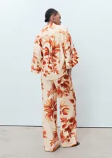 Pantalón de mujer de tejido fluido con estampado de palmeras en tonos naranja y beige. Diseño recto y largo, con tiro medio, dos bolsillos laterales y forro interior.