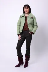Campera corta de poliéster texturizado color verde oscuro, con cuello camisero, cierre frontal con botones a presión, bolsillos delanteros y forro interior. Incluye pins decorativos.