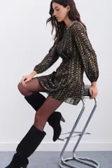 Vestido corto negro con estampado abstracto dorado, escote redondo, mangas largas con elástico en los puños, detalle de nudo drapeado en la cintura y escote en V pronunciado en la espalda.