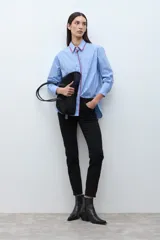 Camisa de manga larga, corte oversize, color celeste con rayas verticales blancas. Presenta un detalle de bordado en color rojo/fucsia a lo largo del cuello y la abertura frontal.