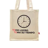 Bolso tipo tote bag de tela color crudo con asas de hombro. Estampado frontal con un reloj y la frase "TODO LOGRO TOMA SU TIEMPO".
