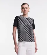 Remera de crepé con estampado geométrico de formas y rayas en blanco y negro. Tiene cuello redondo con borde blanco contrastante y mangas cortas negras.