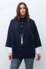 Chaqueta tejida de punto color verde oliva, con cuello alto y cierre frontal de botones a presión. Presenta bolsillos delanteros aplicados y mangas amplias de largo tres cuartos.