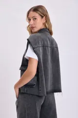 Chaleco de jean negro con cuello camisero, cierre frontal con botones, bolsillos de parche y sisas desflecadas.