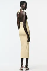 Vestido midi color crema de poliamida con cuello halter con lazada, escote pico pronunciado, detalle de pieza metálica y tejido con frunces.