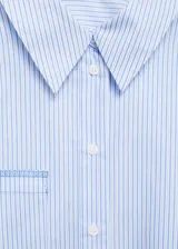 Camisa corta de popelina de algodón a rayas verticales celestes y blancas, con cuello camisero, mangas largas con puños abotonados, bolsillo de parche en el pecho y cierre frontal con botones.