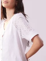 Blusa blanca de algodón con escote en V, abertura con botones y mangas cortas con detalle de broderie.
