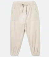 Pantalón jogger color beige, con elástico en la cintura y en los tobillos, cordón ajustable, bolsillos laterales y detalles de agujeros en los laterales y en los bolsillos.